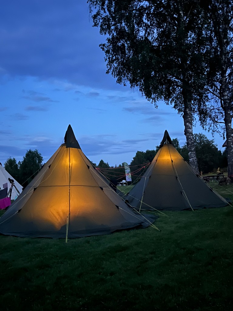 Two lavvos at camp with lights inside. 
