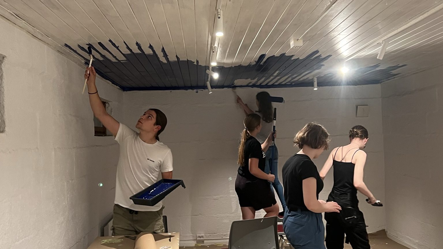 Five rovers painting the ceiling dark blue. To show that you can do a lot more as an adult in scouts than being the traditional scout leader.